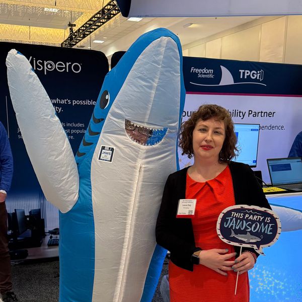 Me with short blond hair, in a red dress, at a conference posing with a person in a shark costume.