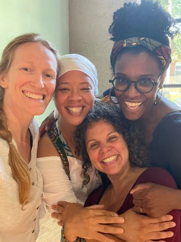 Four diverse women smiling closely together in a warm embrace.