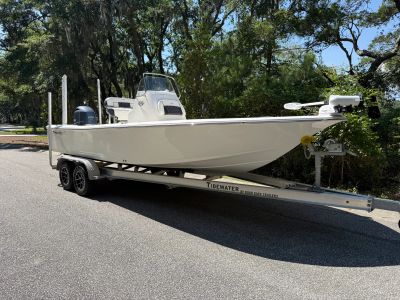 White fishing boat on a trailer parked on a street with trees.