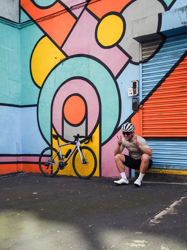 Cyclist posing cheerfully by a colorful geometric mural with his bike.