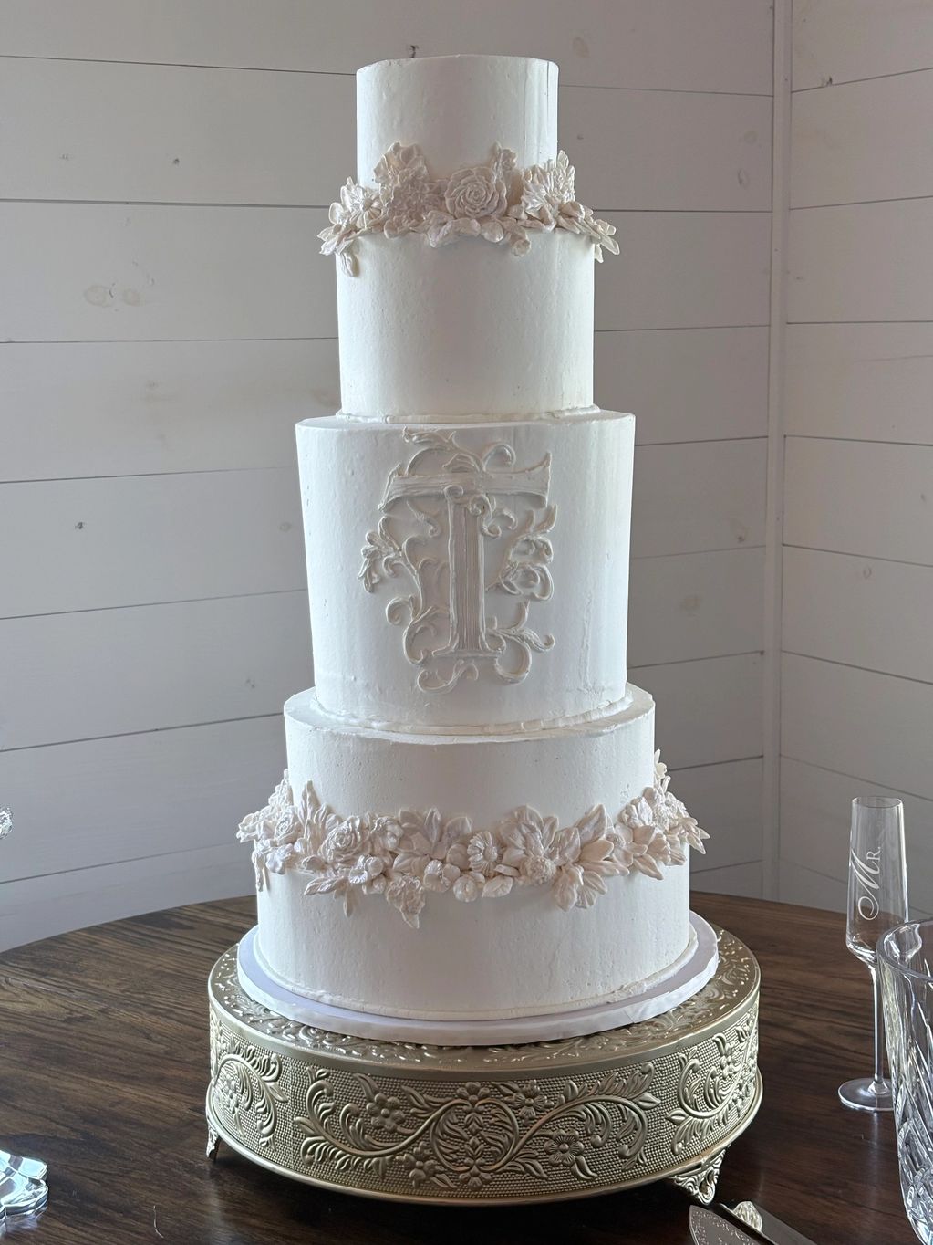 Elegant three-tier white wedding cake with floral decorations and a monogram.