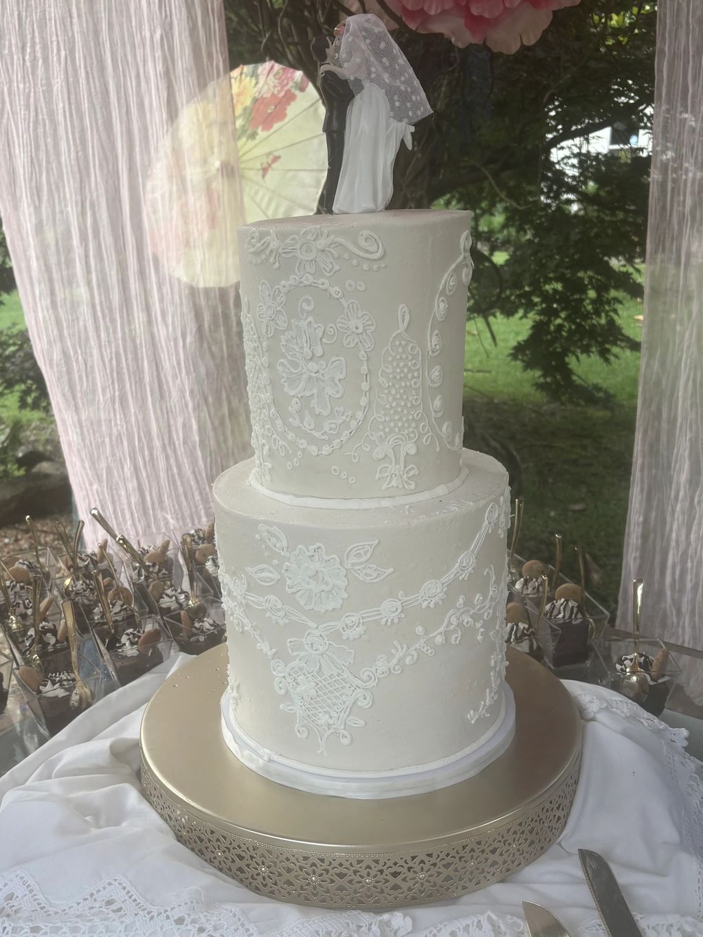 Elegant two-tier white wedding cake with intricate floral icing and bride-groom topper.