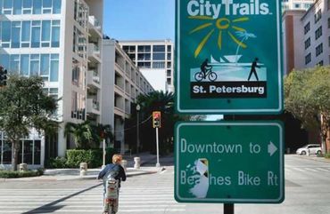 Person rides bike near St. Petersburg City Trails signs in urban area.