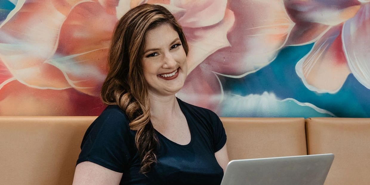 Smiling woman with laptop against a floral mural.