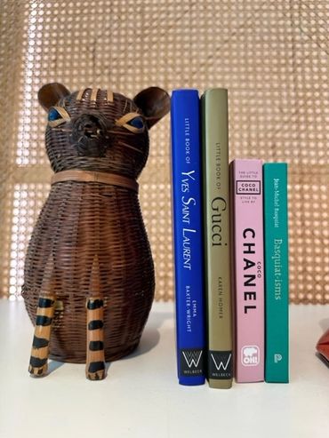 Stack of books with a vintage rattan cat dressing up a shelf at Frances Vallentine