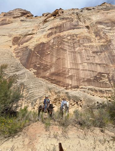 Two riders sit on mules in front of a towering canyon wall in southern Utah