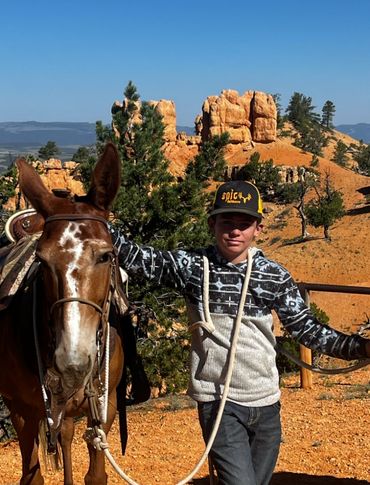 A young man poses with a mule in front of orange hoodoos