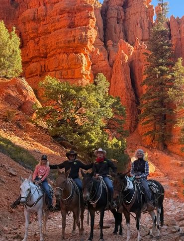 A group of friends gather together on the backs of mules to pose in front of hoodoos in Red Canyon