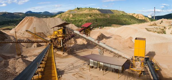 A large sand and gravel quarry with conveyor belts and machinery under a blue sky.