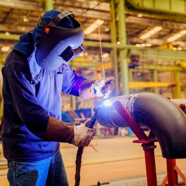 A welder working on a large metal pipe in an industrial factory.