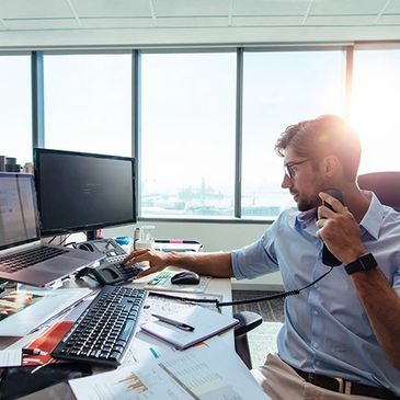 Man multitasking at a modern office desk with multiple screens and documents.