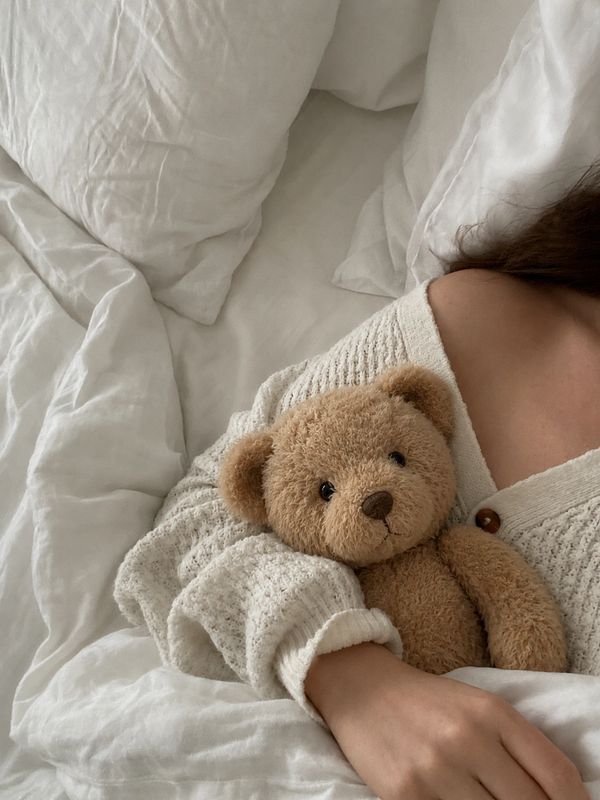 Person holding a teddy bear in bed.