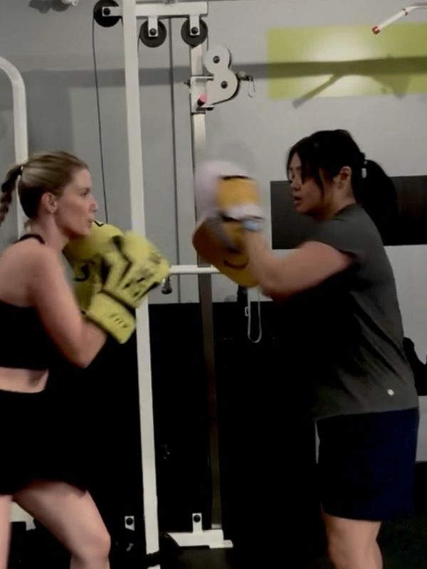 Two women boxing in a gym with yellow gloves and focus mitts.