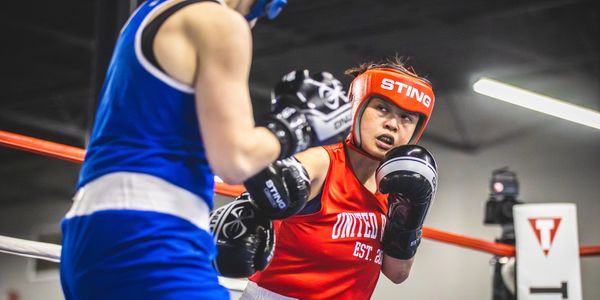 Two boxers sparring in a boxing ring, one in red and the other in blue.