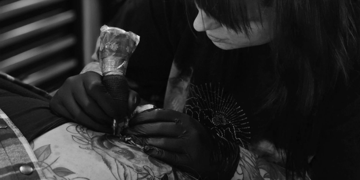 Tattoo artist intensely working on a detailed deer tattoo in black ink.