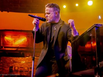 Male singer passionately performing on stage with vibrant lighting.
