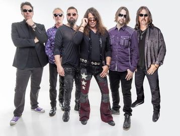 A rock band poses confidently in stylish attire and sunglasses against a white backdrop.