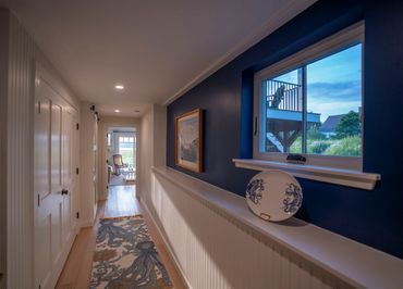 Cozy hallway with blue accent wall, decorative plate, and wooden flooring leading to a sunlit room.