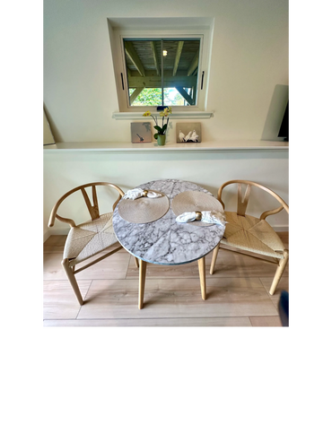 Minimalist dining area with a round marble table and two wooden chairs.