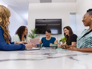 Business branding photo with women in a white office meeting smiling wearing blue and teal