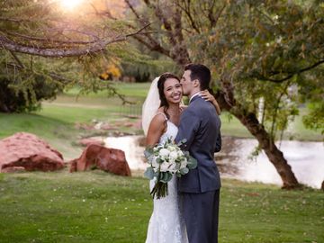 Wedding couple photoshoot with groom in grey and kissing bride with bouquet in Sedona, AZ by red roc