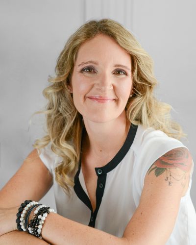 Femme souriante aux cheveux blonds avec un tatouage et des bracelets.