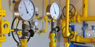 Industrial pressure gauges attached to yellow pipes in a facility.