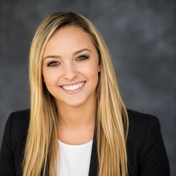 Professional woman with blonde hair smiling against a gray backdrop.