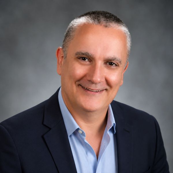 Smiling middle-aged man in business attire against a gray background.