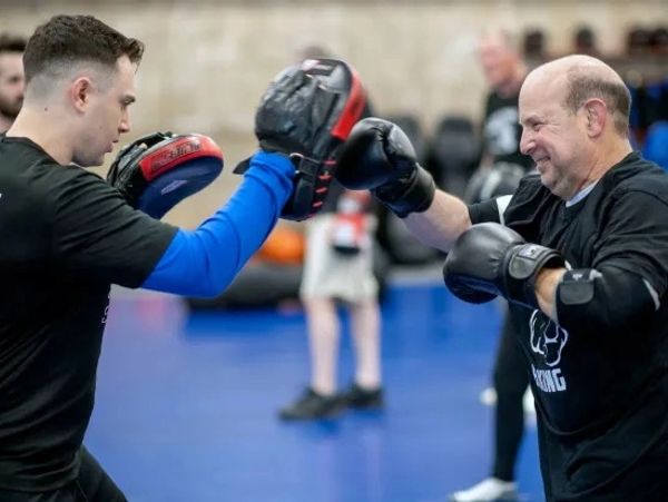 Two men practicing boxing with gloves and pads in a gym.