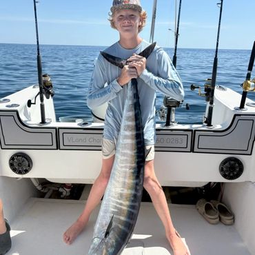 A young boy proudly holds a large fish on a boat during a sunny day at sea.