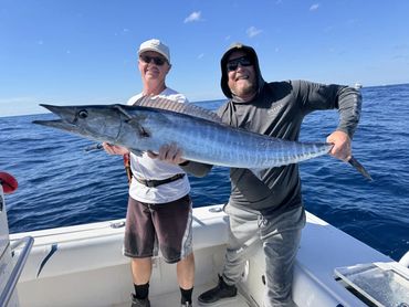 Two men proudly holding a large fish on a boat in the ocean.