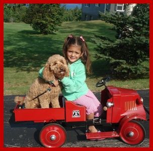 A young girl riding a toy truck with her Australian labradoodle