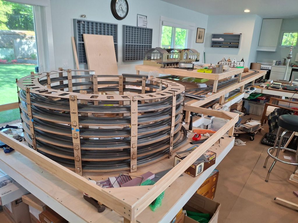 Large wooden model train layout under construction in a bright room.