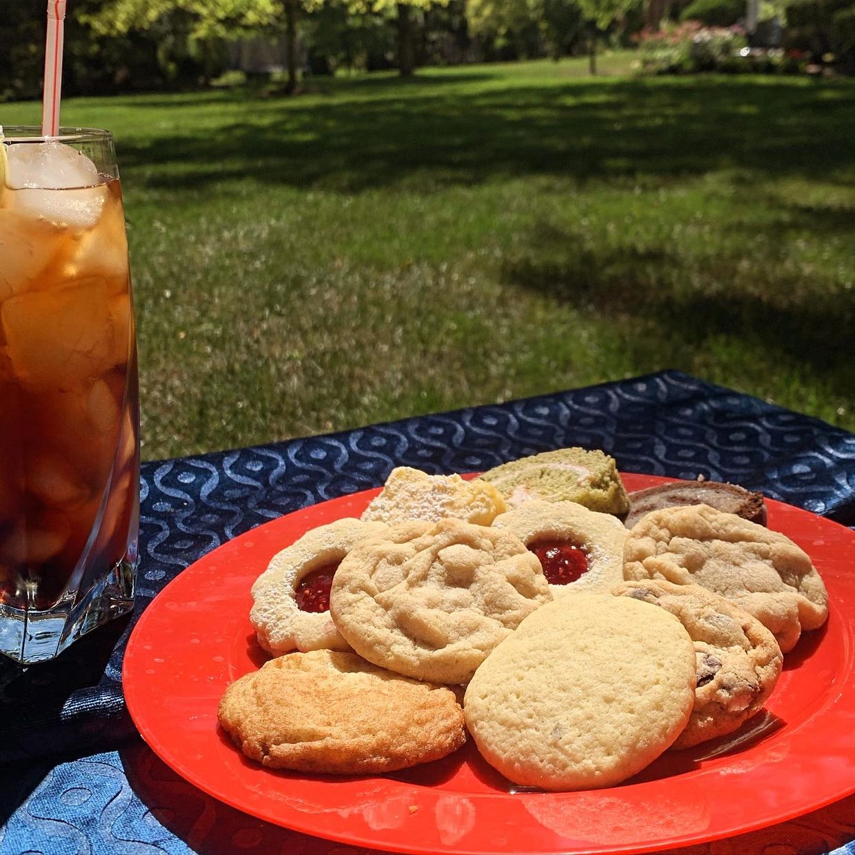 Plate of assorted cookies with iced tea outdoors.