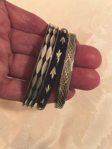 Hand holding three intricately designed silver and black bangles.
