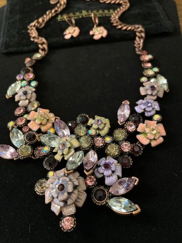 Floral statement necklace and earrings with pastel gemstones on black velvet.
