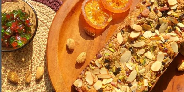 A nut and fruit topped cake with sliced almonds and dried orange slices on a wooden plate.