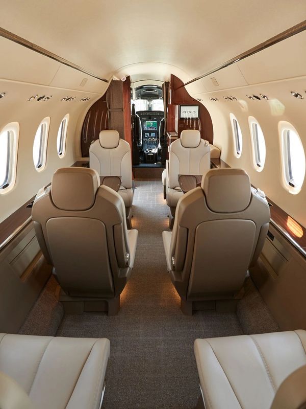 Luxurious interior of a private jet with beige leather seats and wood accents.