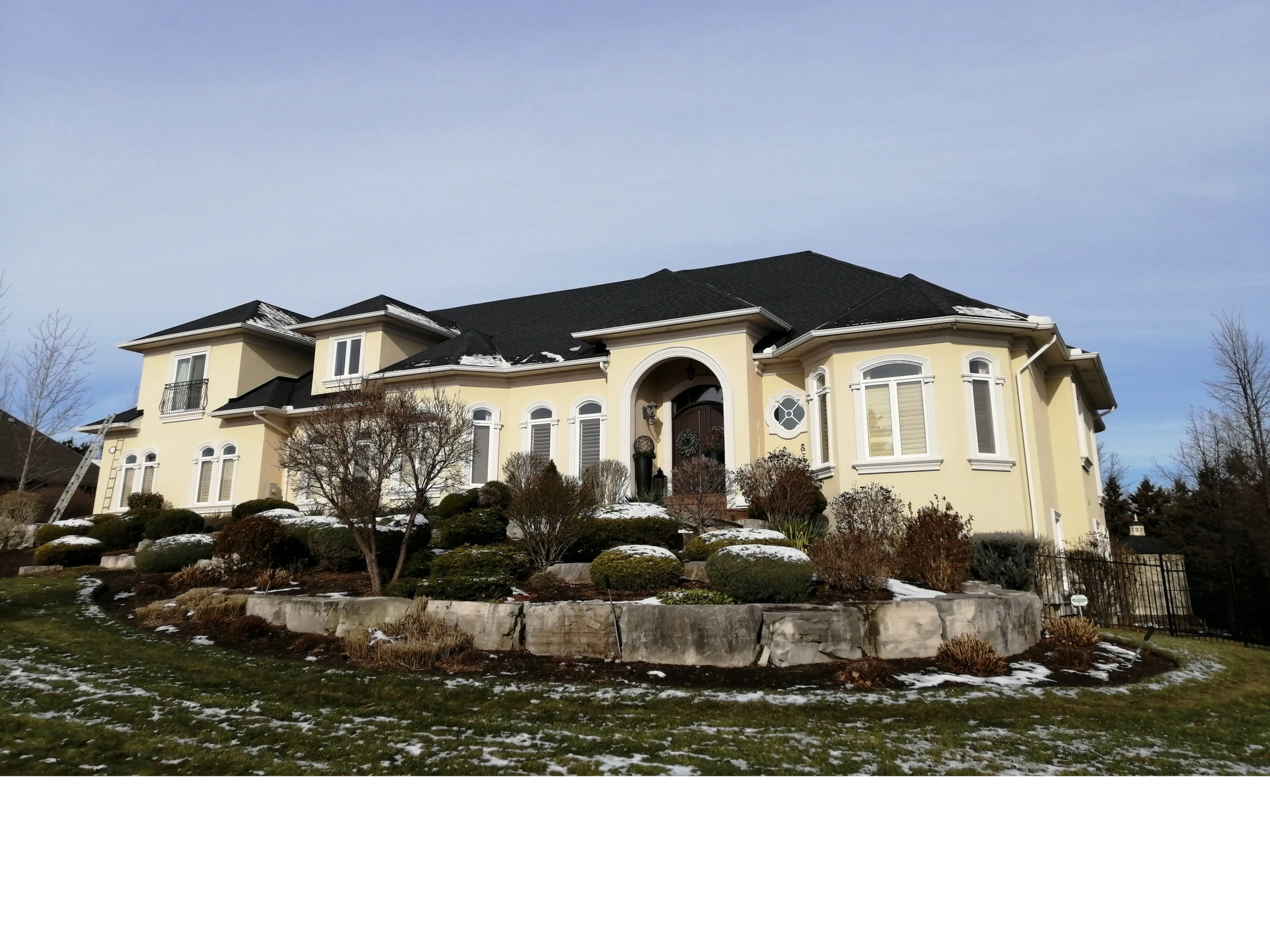 Large beige house with black roof and winter landscaping.