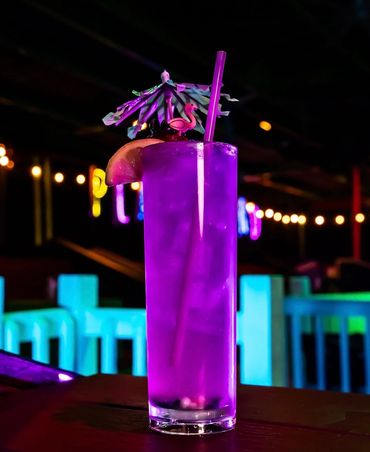 Vibrant purple cocktail with festive garnish in a lively bar setting.