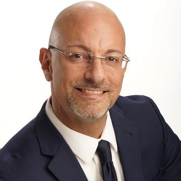 A photo of Dr. Lonnie Herman, wearing a black suit and black tie, smiling.