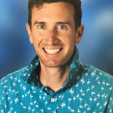 Smiling man in a blue flamingo-patterned shirt against a blue background.