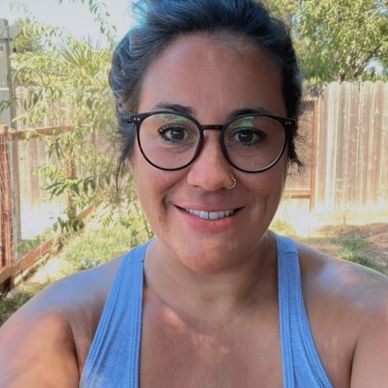Smiling woman in glasses and a blue tank top outdoors on a sunny day.