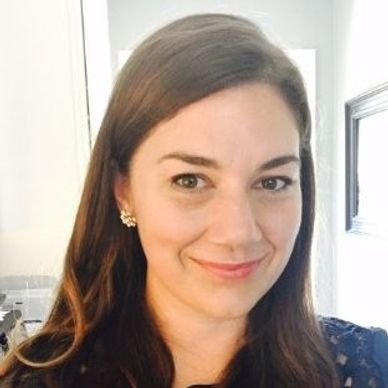 Smiling woman with long brown hair in a softly lit room.