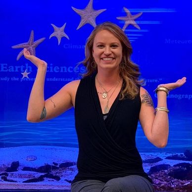 A smiling woman poses with starfish in an aquarium exhibit.
