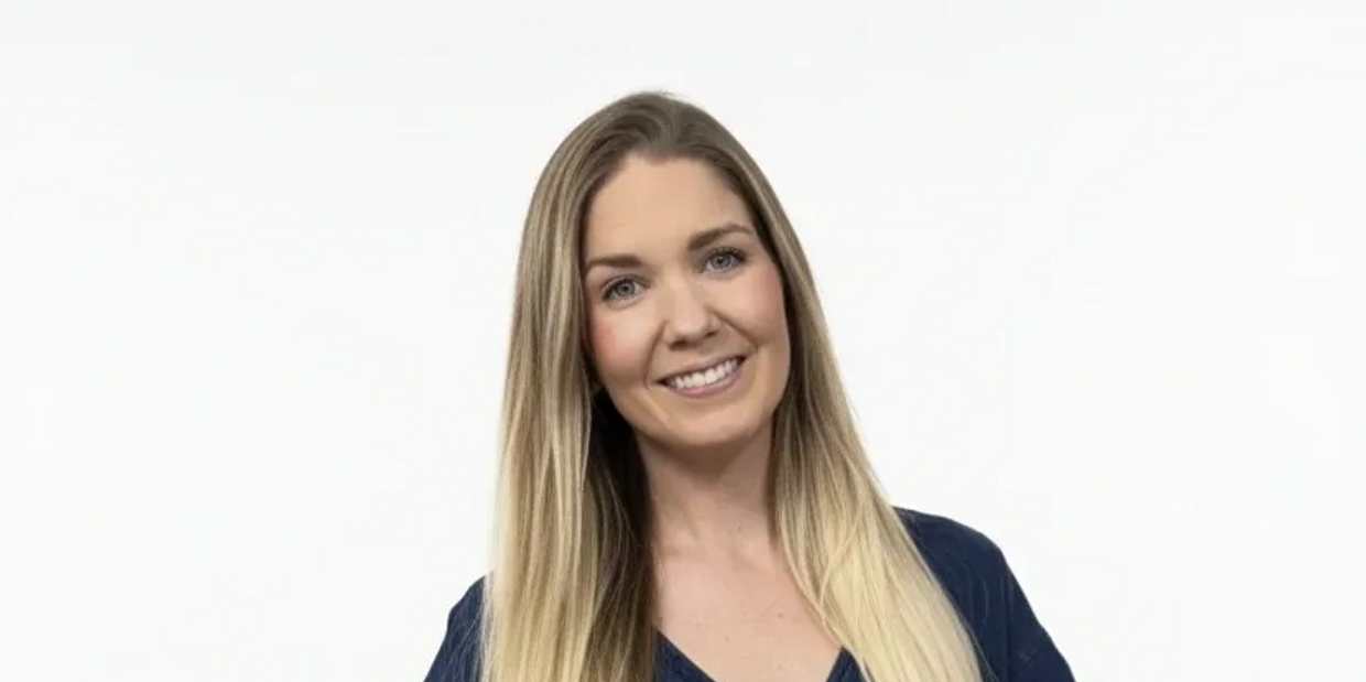 Young woman with long blonde hair in a navy shirt smiles against a white background.