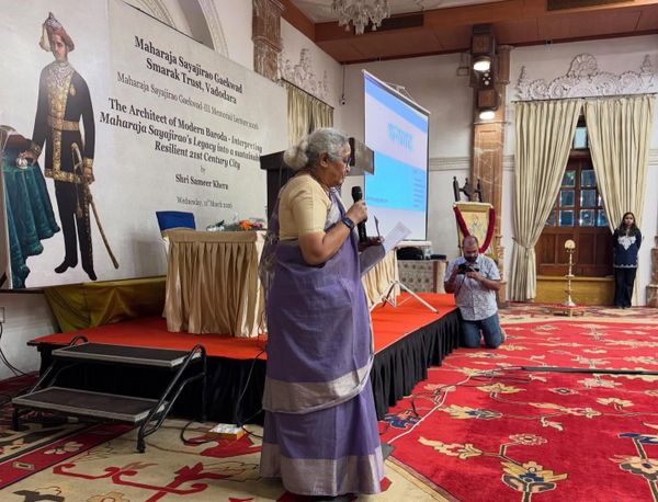 A woman in traditional attire speaking on stage at a cultural event.