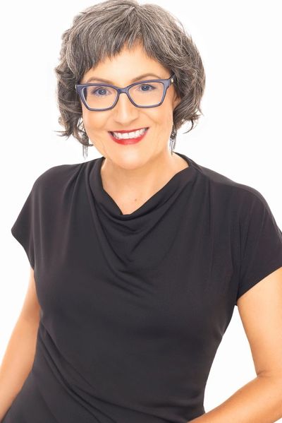 Smiling woman with glasses in a black top against a white background.