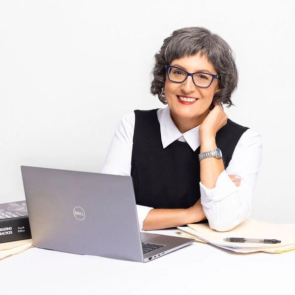 Smiling professional woman with glasses working on a laptop at a desk.